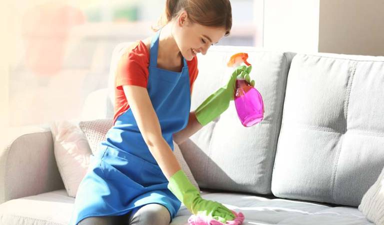 Woman in red blue dress holding a pink bottle and scrubbing her sofa