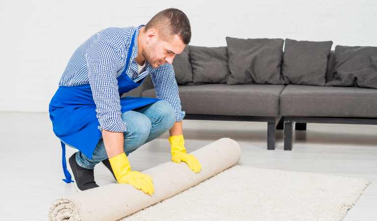 Professional cleaner in uniform folding carpet