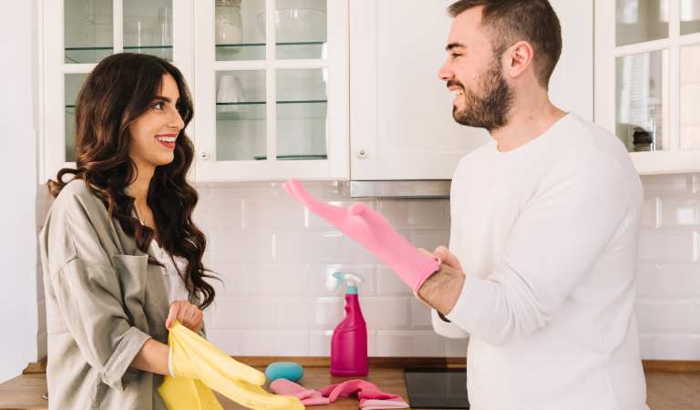 Woman earing yellow glove and a man wearing pink glove inside a kitchen.