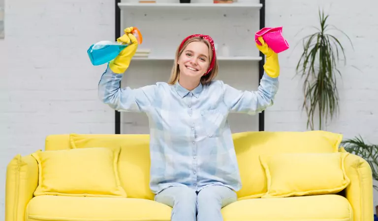 young woman looking happy and sitting on a couch with some cleaning supplies