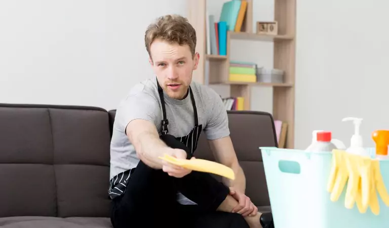 young man with some cleaning supplies sitting inside of a house