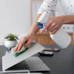 Woman holding a white spray bottle cleaning her laptop