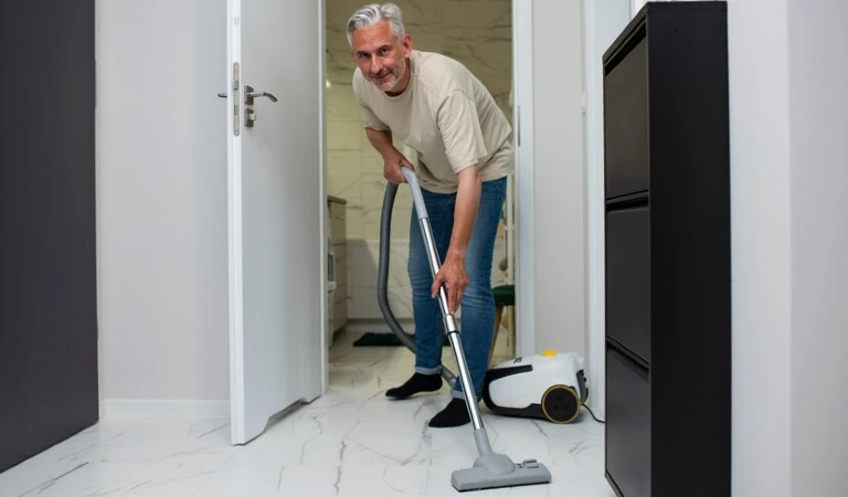 Old man cleaning floor with a vacuum cleaner.