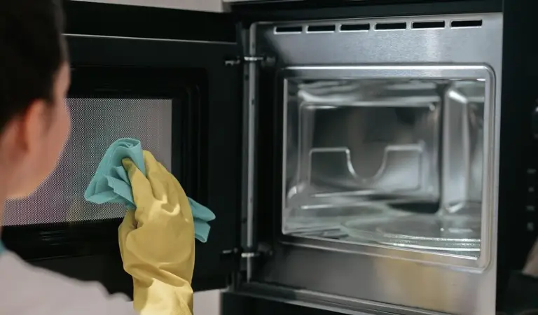 Woman in yellow gloves cleaning oven with a blue cloth.