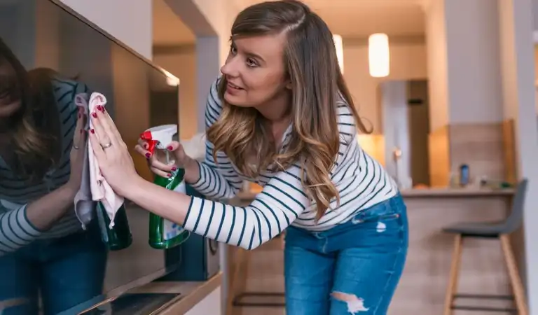 Lady in jeans top cleaning her television with a cloth.