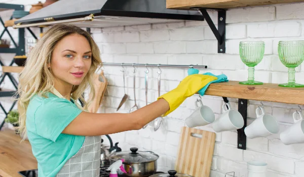 Young woman wiping kitchen shelf looking at camera