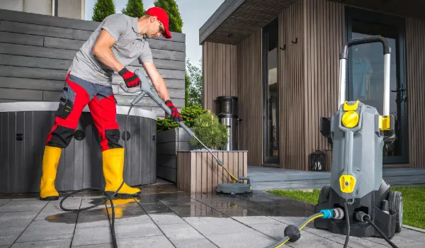 Caucasian worker power washing patio concrete bricks using professional pressure washer