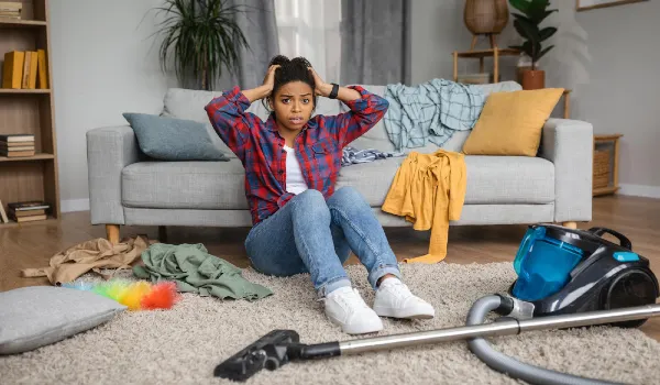 Despaired sad tired confused millennial black housewife hold head with hands sit on floor with vacuum cleaner