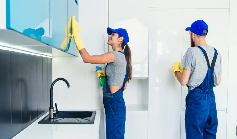 Professional man and woman cleaners in blue work uniform cleaning the furniture with rags and spray in the contemporary kitchen