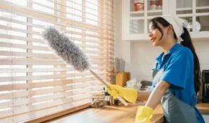 Asian woman with duster cleans dirty window blinds enjoying housework ensuring hygiene for a modern clean home