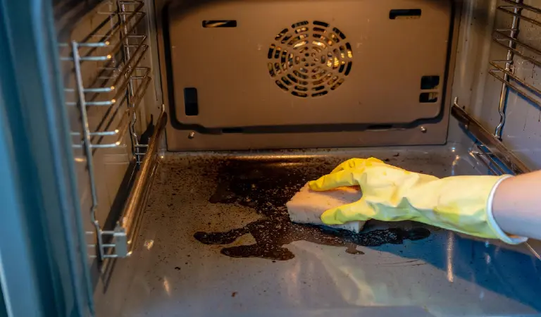 Hand in rubber glove cleaning dirty oven with sponge and cleaner housework and housekeeping concept