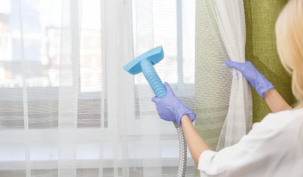 The girl holds a steamer for curtains in her hand cleaning of the apartment