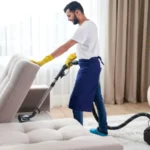 Young man cleaning sofa with vacuum cleaner in leaving room at home