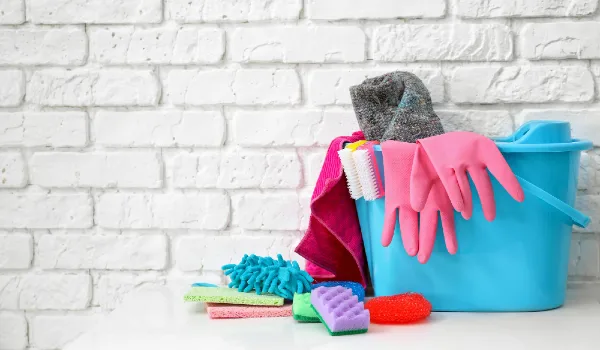 Bucket with cleaning supplies and tools on table near brick wall