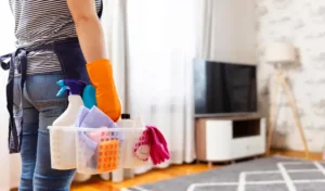 Woman in rubber gloves with basket of cleaning supplies ready to clean up