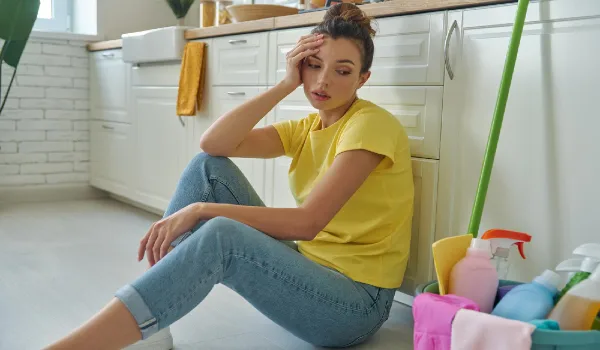 A woman sits on the floor in a kitchen with a basket of laundry baskets