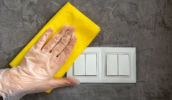 Woman clean light switch with cloth on gray concrete wall. Hand in glove disinfecting surfaces by yellow rag